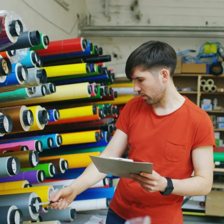 A man in red t shirt examining rolls of vinyl on racks
