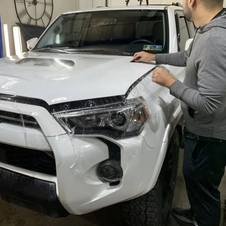 Man applying paint protection film to car hood.
