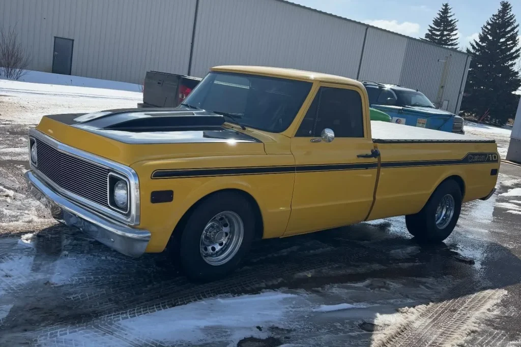 A classic yellow truck with black wrapped hood and striping on down the side.